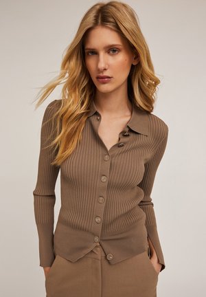 Bruine geribbelde cardigan met een knoopsluiting aan de voorkant, voorzien van een kraag, lange mouwen en zijsplitten. Soepele textuur met zes bijpassende knopen.