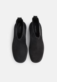 Černé nazouvací boty s hladkým semišovým svrškem, elastickými bočními panely a designem zaoblené špičky, s viditelným logem na stélce.