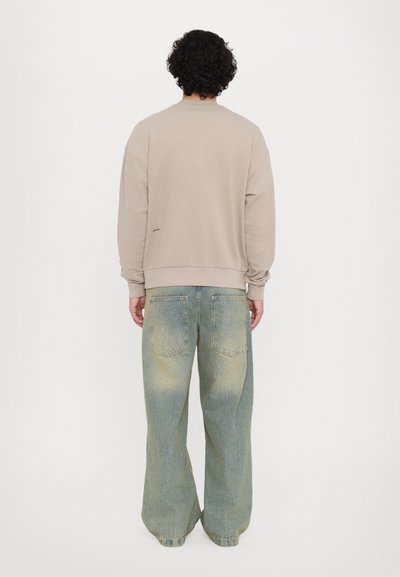 Light beige sweatshirt with a relaxed fit, crew neckline, and ribbed cuffs. Paired with light blue, wide-leg, acid-washed jeans.