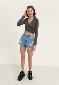 Sivi dugi rukavi crop top s dizajnom omota, uparen s iznošenim plavim trapericama. Model nosi crne masivne tenisice.