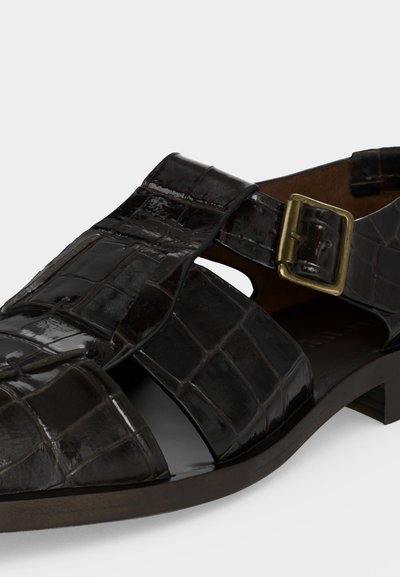 Μαύρο γυαλιστερό δερμάτινο σανδάλι με υφή κροκόδειλου, ανοιχτή μύτη και ρυθμιζόμενο μπρούτζινο λουράκι με αγκράφα σε χαμηλό ξύλινο τακούνι.