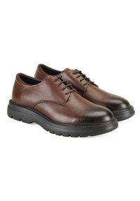 Bruine leren schoenen met een gestructureerde afwerking, ronde neus en zwarte rubberen zool met opvallende noppen. Veters zichtbaar op de bovenkant.