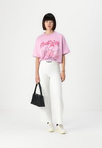 Pink oversized t-shirt with graphic print, white high-waisted pants, black handbag, and cream sneakers. Smooth texture and relaxed fit.