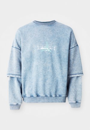 Blå bomullsgenser med senkende skuldre, ribbestrikket halslinning og broderte detaljer. Har en løs passform og teksturert stoff.