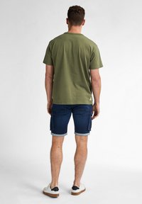 Olive green cotton t-shirt with short sleeves, paired with dark denim shorts featuring cargo pockets and rolled hems. Casual white sneakers.