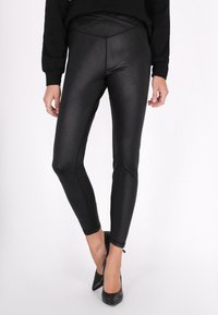 Fekete, magas derekú leggings fényes, elasztikus anyagból. Formázott fazon, varrás nélküli oldalakkal és sima textúrával, fekete magassarkú cipővel párosítva.