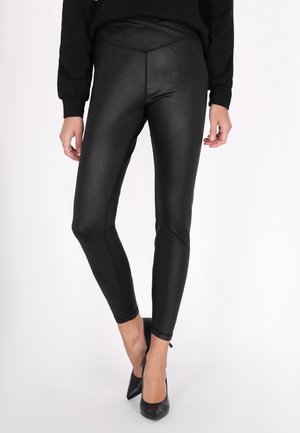 Zwarte, high-waisted legging van een glanzende, rekbare stof. Aansluitend ontwerp met naadloze zijkanten en een gladde textuur, gecombineerd met zwarte hakken.