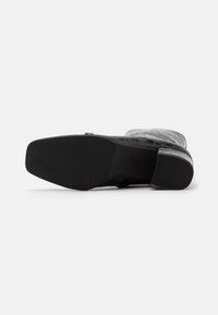 Zapato de cuero negro con un patrón texturizado similar al de un cocodrilo. Suela de goma plana con punta cuadrada y talón contorneado. Diseñado para la comodidad y la durabilidad.