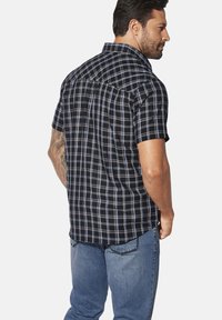 Kurzärmliges, kariertes Hemd in Marineblau mit weißen und hellblauen Linien. Weicher Stoff, Kragen, Rückenpasse und lockere Passform. Kombiniert mit blauen Jeans.