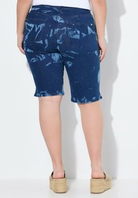 Pantaloni Bermuda in denim blu scuro con motivo tie-dye. Presentano cinque tasche, una finitura liscia e un orlo dritto. Indossati con sandali con zeppa.