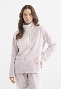 Suéter de forro polar en rosa suave con un cuello alto y cremallera. Presenta patrones de sol y luna. Tejido texturizado con una apariencia acogedora y suave.