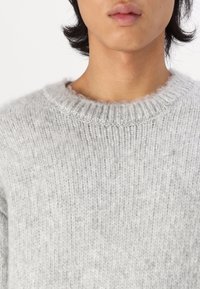Maglione grigio chiaro a maglia con scollatura rotonda, realizzato in materiale morbido e testurizzato, con un sottile motivo a coste sul collo.