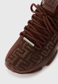 Sneaker marrone con tomaia in mesh testurizzato caratterizzata da un motivo geometrico e decorazioni scintillanti. Include lacci piatti marroni e un'etichetta con logo metallico.