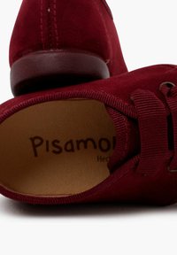 Scarpa in suede bordeaux con punta rotonda, chiusura con lacci e interno morbido. Presenta un logo in rilievo e una suola in gomma testurizzata.