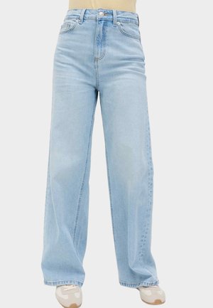 Lyseblå vidde jeans med høj talje, båret med hvide sneakers, med forlommer, bæltestropper og knaplukning.