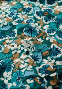 Green fabric with a floral print featuring white, blue, and brown flowers, displaying a soft texture and wavy pattern.