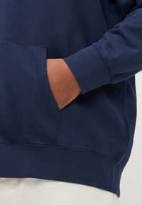 Navyblå genser laget av bomullsblanding, med kengurulomme, ribbede mansjetter og nederkant, samt en glatt, teksturert finish.