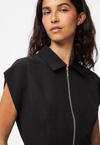 Vestido preto de manga curta com gola e um fecho metálico à frente. Feito de um tecido suave com um corte estruturado.