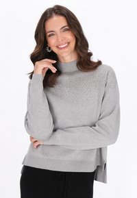 Pulover gri cu guler înalt, având un model subtil de strasuri la umăr. Margine ondulată și fante laterale în partea de jos.
