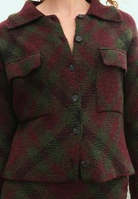Wool blend jacket in plaid pattern with dark green and burgundy hues. Features a collar, two chest pockets, and black buttons.