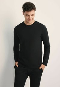 Czarna koszulka z długim rękawem, wykonana z bawełny, z okrągłym dekoltem, dopasowanym krojem i subtelnym logo na piersi.