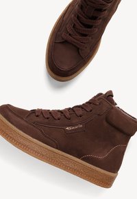 Zapatillas altas de cuero marrón con cordones a juego, suela de goma texturizada y detalles de costura sutiles. El nombre de la marca "Tamaris" es visible.