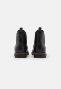 Bottines en cuir noir avec une finition lisse, un talon empilé, des coutures contrastées et des languettes à l'arrière pour un enfilage facile.