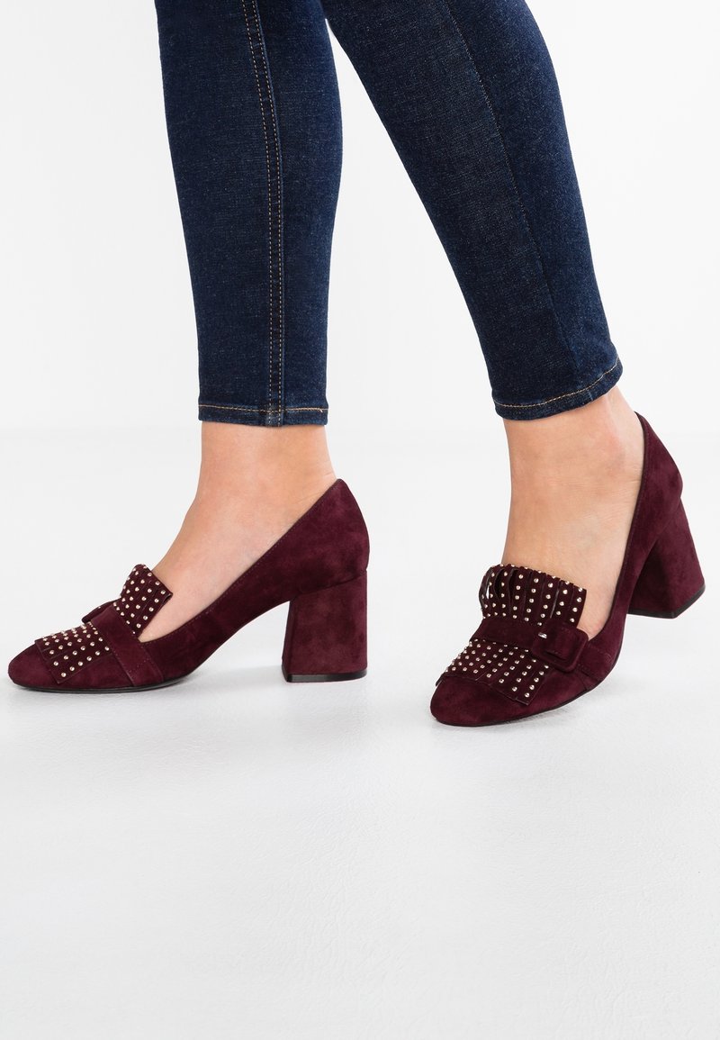 Chaussures à talons hauts en daim bordeaux avec un nœud décoratif et des accents cloutés sur la pointe, dotées d'un talon bloc pour la stabilité.
