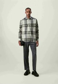 Rutete flanellskjorte med svart og hvitt mønster, med knapplukking foran; kombinert med mørkegrå skreddersydde bukser og svarte joggesko.