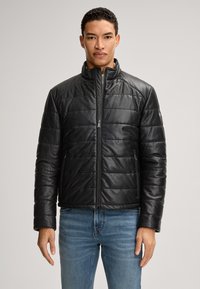 Schwarze Lederjacke mit gestepptem Design, hohem Kragen und Reißverschluss. Begleitet von blauen Jeans, präsentiert an einer Person.