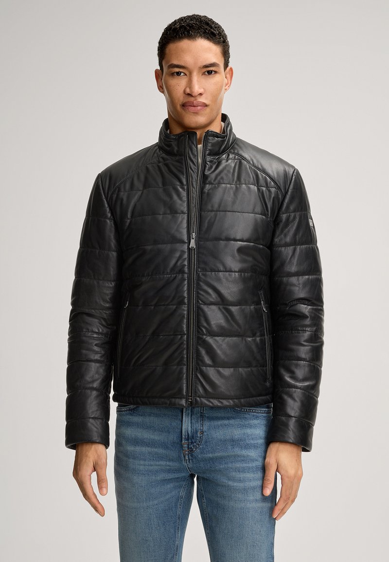 Schwarze Lederjacke mit gestepptem Design, hohem Kragen und Reißverschluss. Begleitet von blauen Jeans, präsentiert an einer Person.