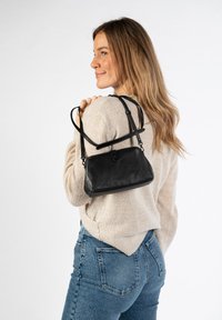 Borsa a tracolla nera in pelle con forma strutturata e manico corto, dotata di chiusura a scatto e superficie liscia. Indossata sopra un maglione chiaro.