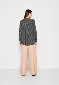 Black and white striped shirt with long sleeves, paired with wide-leg, pale pink trousers. Minimalist design, smooth textures, casual fit.