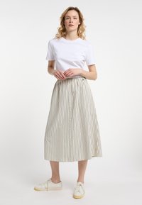 Hvid bomulds T-shirt kombineret med en knælængde, beige nederdel med sorte lodrette striber og knaplukning foran. Hvide sneakers.