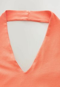 Koraal V-hals top gemaakt van zachte stof met een gladde textuur. Heeft een brede halslijn en een schoon, eenvoudig ontwerp.