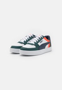 Grønne og hvite joggesko med marineblå og oransje detaljer. Glatt skinn og perforert tåboks. Tykk hvit såle og snøring foran.