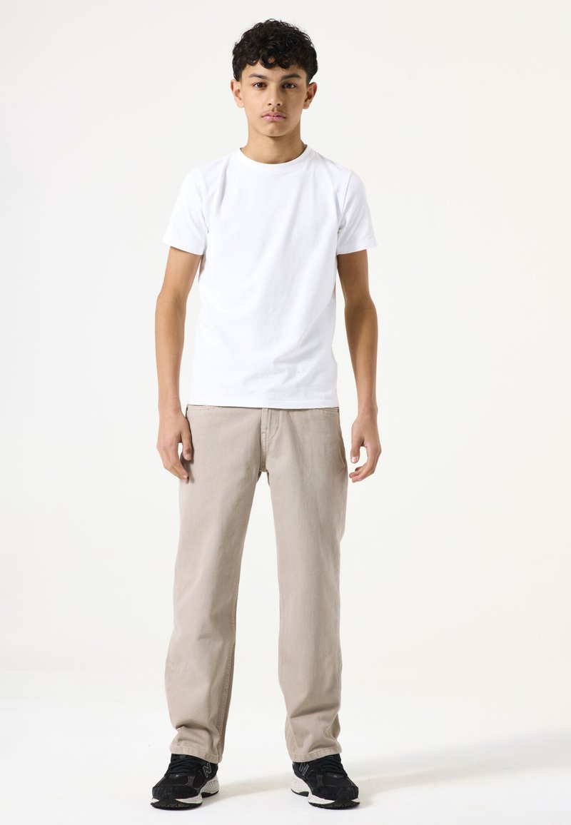 Weißes T-Shirt mit kurzen Ärmeln, kombiniert mit beigen, geraden Hosen und schwarzen Sportschuhen. Schlichtes Design und einfarbige Optik.