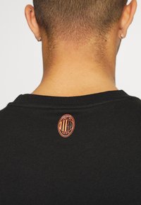 Sweatshirt nero a girocollo caratterizzato da un tessuto testurizzato, con un logo ovale arancione ricamato vicino al collo.