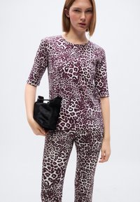 Σετ ρουχισμού με λεοπάρ σχέδιο που αποτελείται από εφαρμοστή μπλούζα με κοντά μανίκια και αντίστοιχα κολάν, σε αποχρώσεις του ροζ, μοβ και εκρού. Κρατά μια μικρή μαύρη τσάντα.