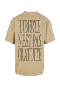 Tricou din bumbac bej, cu text negru, îndrăzneț și uzat pe spate: "LIBERTÉ N'EST PAS GRATUITE." Croi lejer, mâneci scurte, guler rotund.