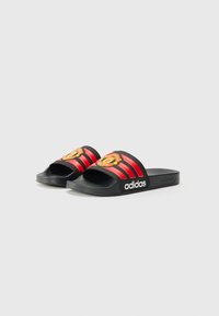 Black slide sandals with red striped accents, featuring a logo and a textured footbed for grip. Made predominantly of rubber material.