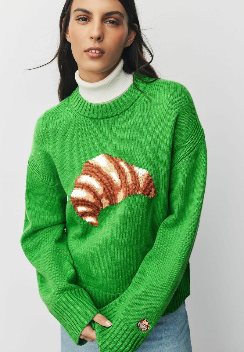 Zaļš adīts džemperis ar kruasāna dizainu brūnā un krēmkrāsā priekšpusē, ar ribotām aprocēm un mazu logotipu uz piedurknes.
