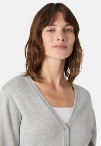 Světlé šedé cardigan vyrobené z měkké pleteniny, se ?-výstřihem, dlouhými rukávy a zapínáním na knoflíky vpředu, s jemným strukturovaným detailem.