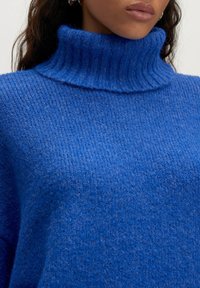 Blauer Strickpullover mit hohem geripptem Kragen und einer weichen, strukturierten Oberfläche. Hat eine lockere Passform und gleichmäßige Nähte.