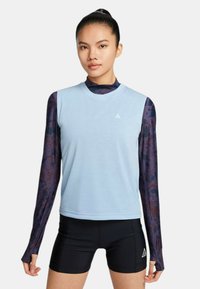 Top atlético azul claro de mangas cortas sobre una capa de manga larga con un patrón oscuro; pantalones cortos negros con acentos laterales.