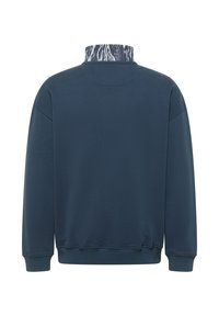 Laivastonsininen svetari, jossa on ribbineulos ja korkea kaulus monivärisellä abstraktilla kuviolla. Pitkät hihat ja rento istuvuus.