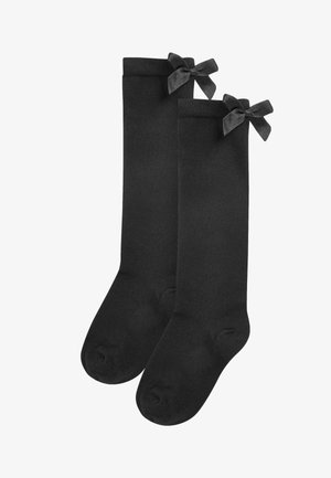 Calze nere al ginocchio realizzate in un tessuto morbido e liscio, con eleganti fiocchi in satin nero decorativi sulla parte superiore di ciascuna calza.