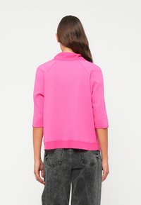 Felle roze sweatshirt met driekwart mouwen, een hoge kraag en ribgebreide zoom, gecombineerd met hoge zwarte spijkerbroek. Gladde textuur.