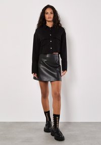Czarna skrócona koszula z przednimi kieszeniami, połączona z czarną skórzaną mini spódnicą o wysokim stanie. Teksturowane czarne buty na platformie i wzorzyste skarpetki.