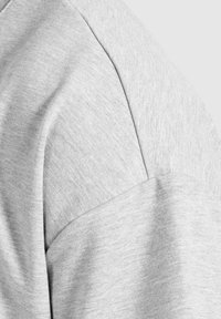 Tessuto del sudore grigio con una texture liscia. Presenta maniche raglan e un delicato motivo melange, mettendo in evidenza un design rilassato.
